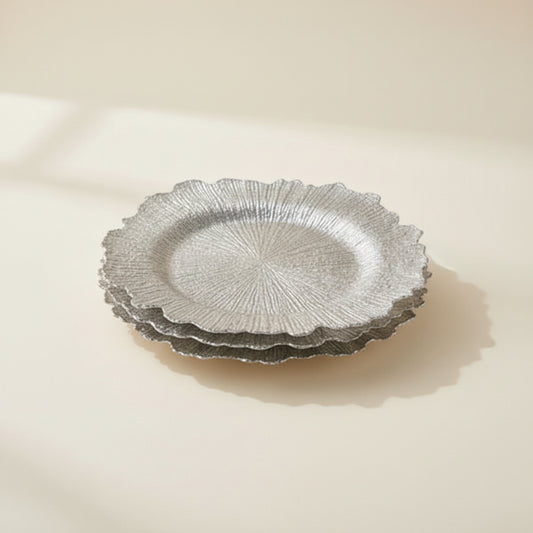 Three-panel collage showing silver-toned textured glass plates: a close-up of a scalloped plate edge, a stack of matching plates on a dark wood surface, and the plates styled on a table with white dinnerware, silver cutlery, flowers, and candles.