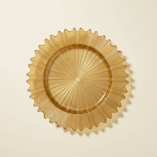 A hand holding a large, round, gold-colored plate or tray with a sunburst, pleated design, set against a warehouse background with cardboard boxes.