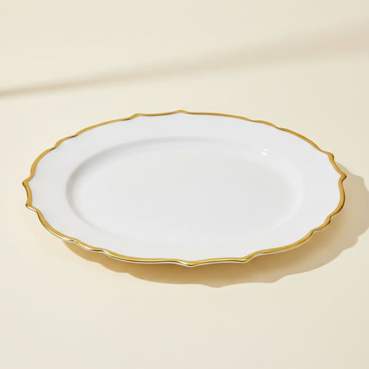 An oval white ceramic serving platter with a delicate, wavy scalloped gold rim, shown against a plain white background.